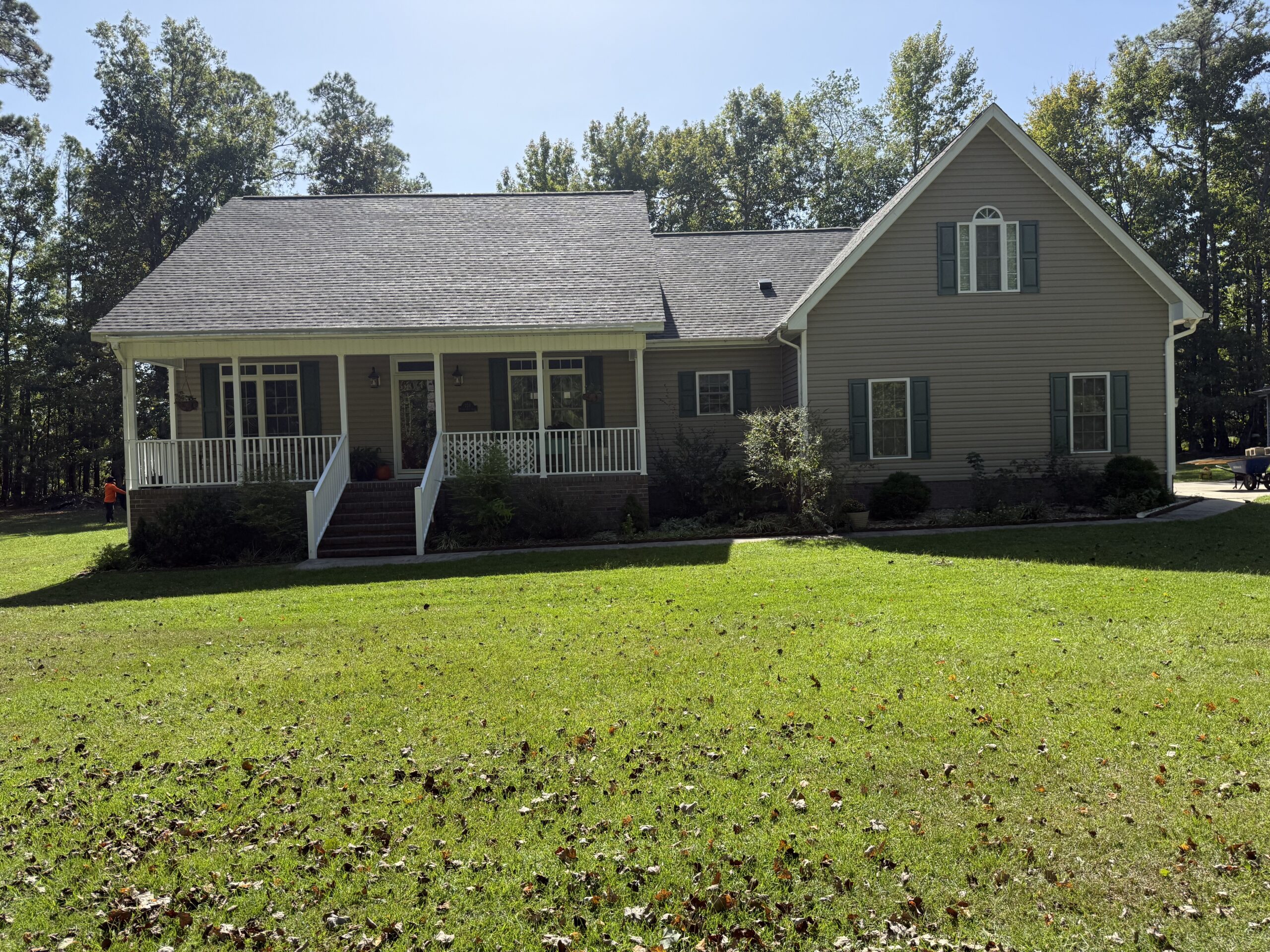 Single-story house with gray siding, white trim, and a covered front porch, set on a grassy lawn with trees in the background.