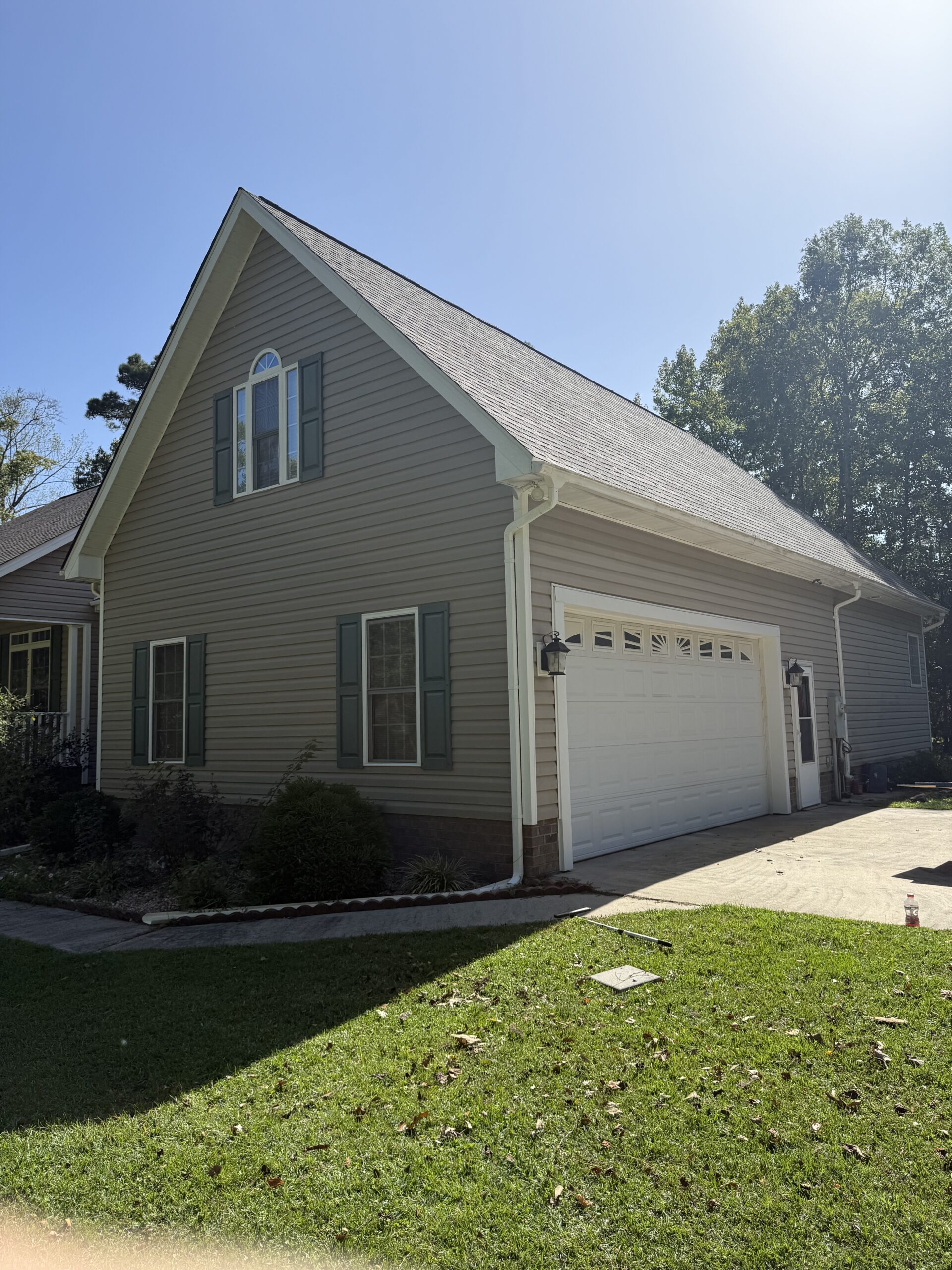 Two-story house with beige siding, green shutters, an arched window, and an attached white garage, situated next to a lawn on a sunny day.